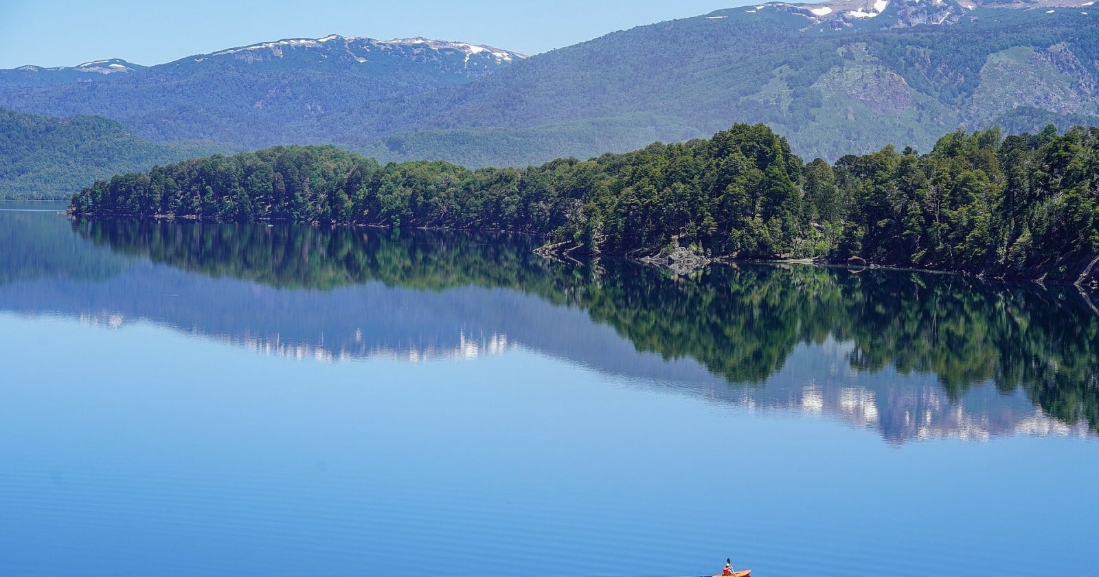 Lago rodeado de bosque y montañas en la zona de Aluminé, con un kayak en el agua
