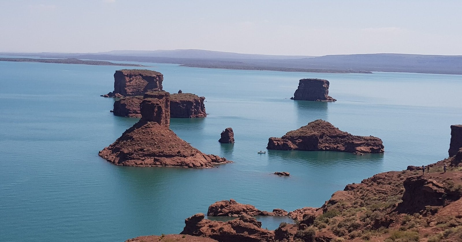 Nadadores con gorras de colores en el agua de la Bahía del Sapo, con las bardas de Villa El Chocón de fondo