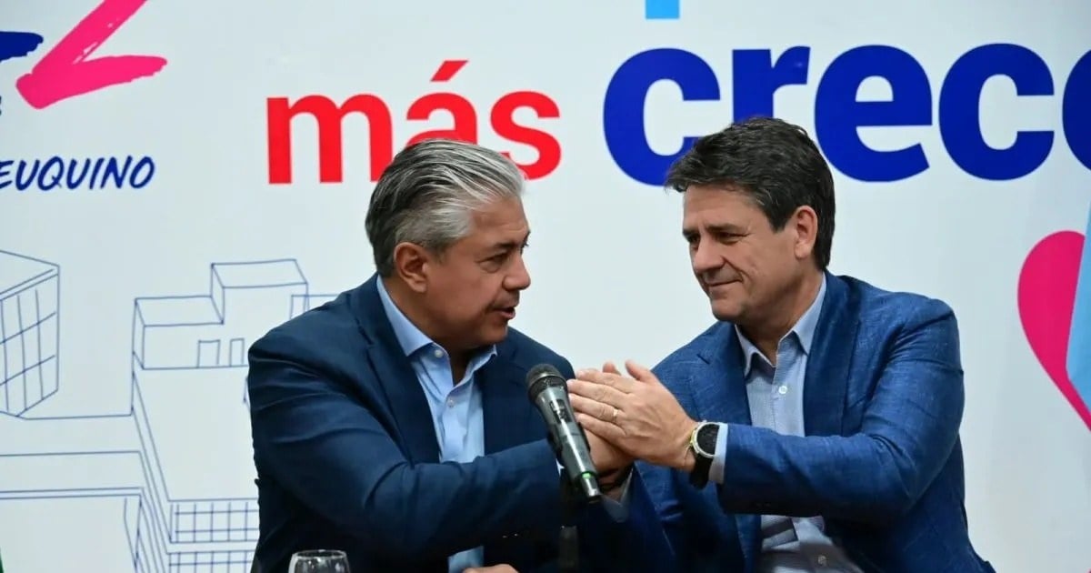 Mariano Gaido se saluda con otro dirigente frente a un micrófono, ante un cartel con la leyenda «más crece»